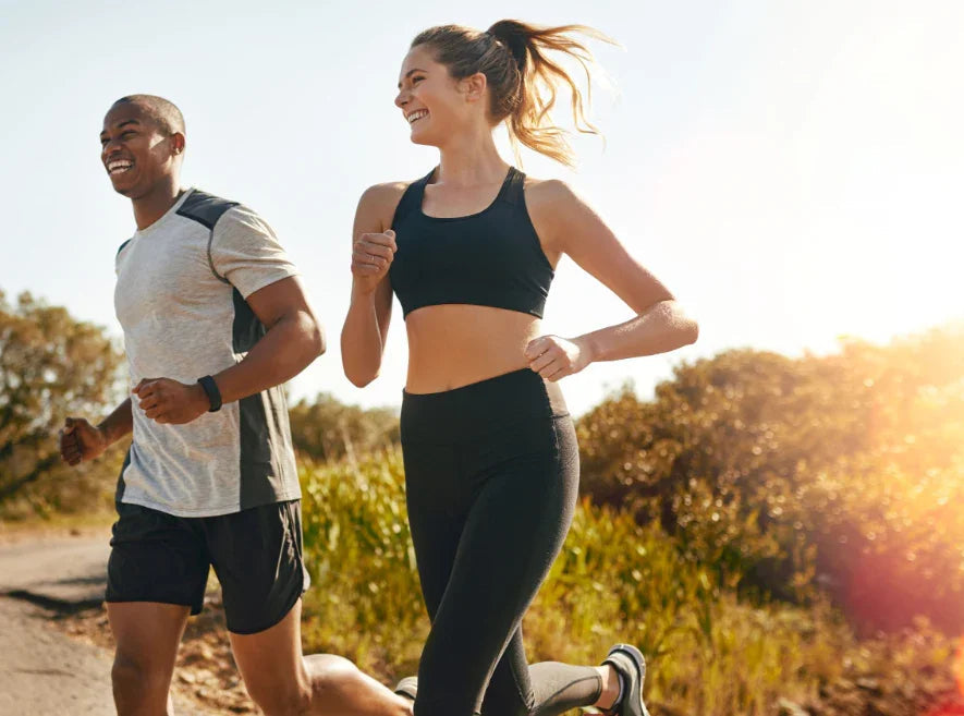 Happy young man and woman jogging outdoors on sunny trail wearing athletic wear